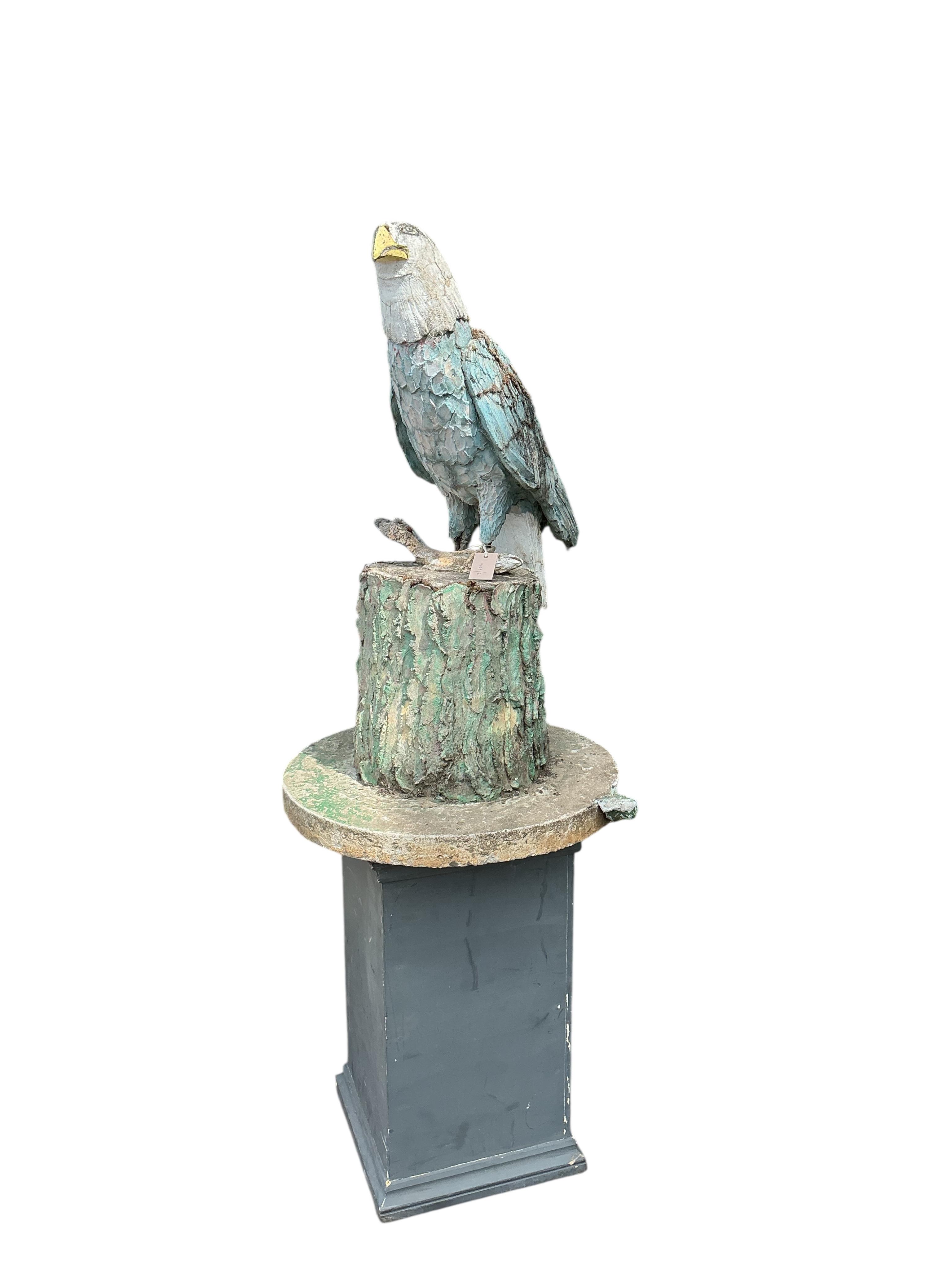 A cast stone garden ornament of an eagle perched on a stump with a salmon in its talons, on square wood plinth, height 150cm